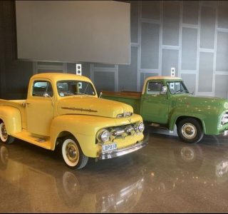 a yellow and green classic car parked inside a high ceiling garage with a polished concrete floor