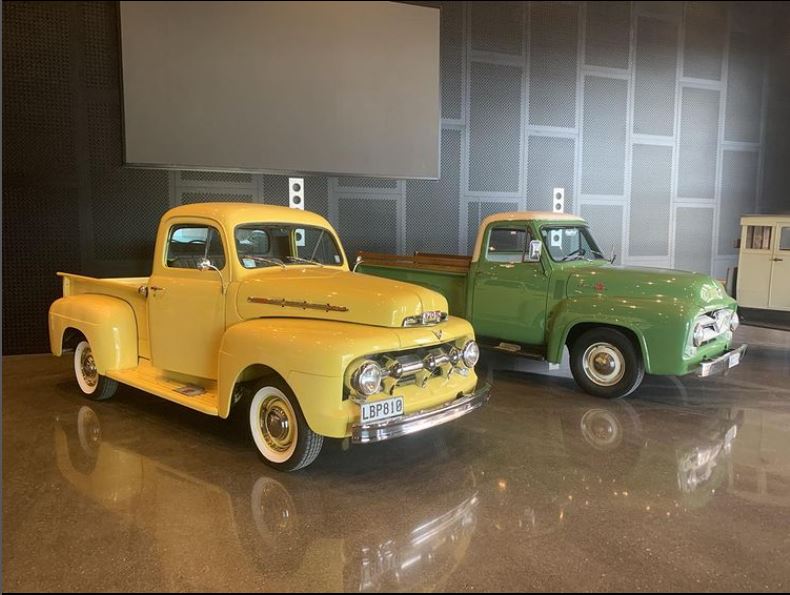 a yellow and green classic car parked inside a high ceiling garage with a polished concrete floor