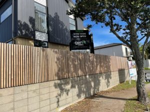 Block honing NZ Grinders Gen X Showhome wooden pailing fence with retaining wall under made of honed concrete blocks in dappled shade of a tree on the footpath and a house behind the fence