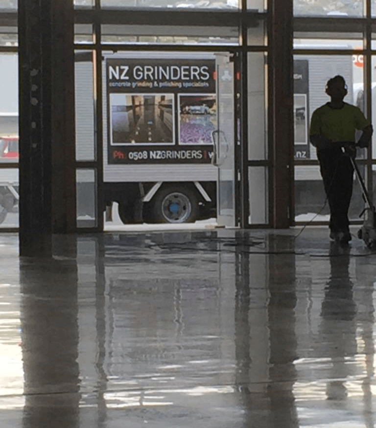 polished concrete floor in a warehouse with a truck in the background shown through glass doors and a worker inside polishing the floor